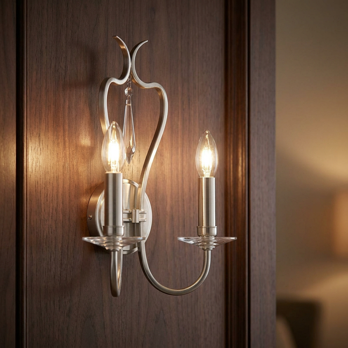 A two-light chrome wall sconce with candle-style bulbs and a crystal droplet mounted on a dark wood panel.