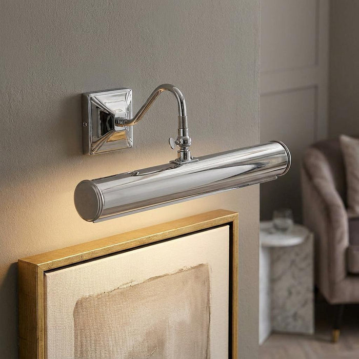 Polished chrome 2 light picture light with a curved arm illuminating a framed artwork on a neutral wall.