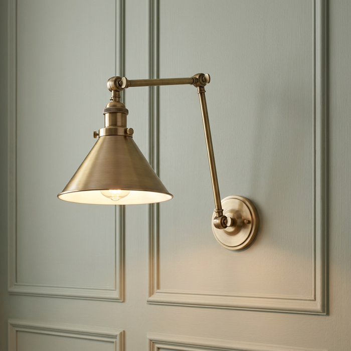 Aged brass swing-arm wall light with a conical shade mounted on a light green paneled wall.