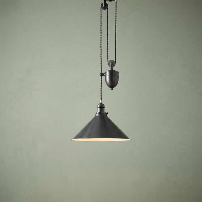 Old bronze rise and fall pendant light with a conical shade and pulley system against a sage green wall.