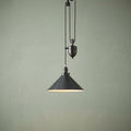 Old bronze rise and fall pendant light with a conical shade and pulley system against a sage green wall.