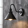 Industrial-style old bronze wall light with a conical shade mounted on a textured grey wall.
