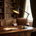 Adjustable old bronze table lamp casting a warm glow on a wooden desk in a traditional library setting.