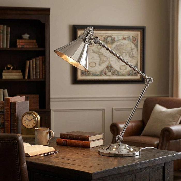 Polished nickel table lamp with an adjustable arm and conical shade illuminating a rustic wooden desk in a study.