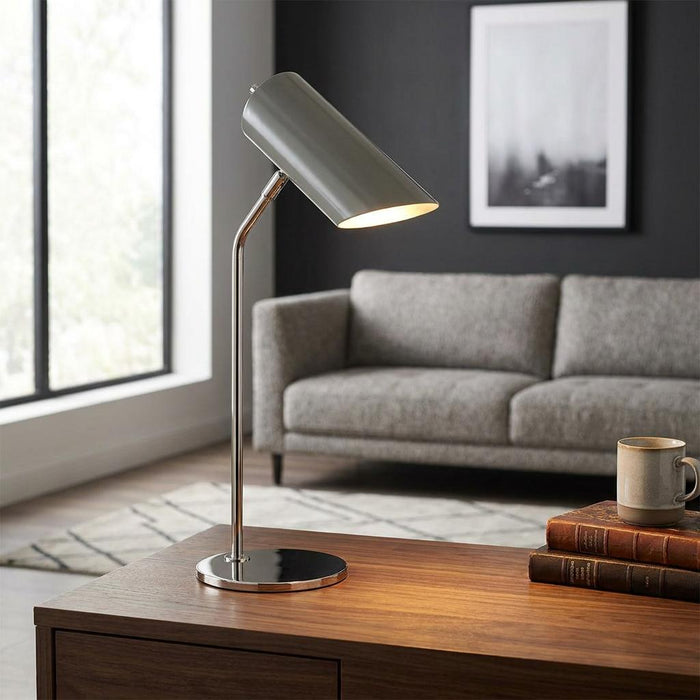 Modern grey and nickel table lamp on a wooden desk in a contemporary living room setting.