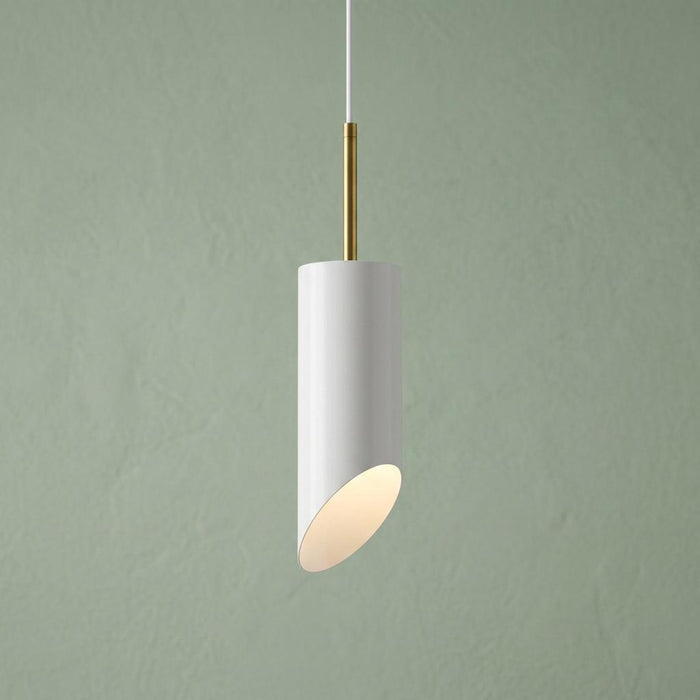 White cylinder pendant light with an angled base and brass stem, glowing against a sage green background.