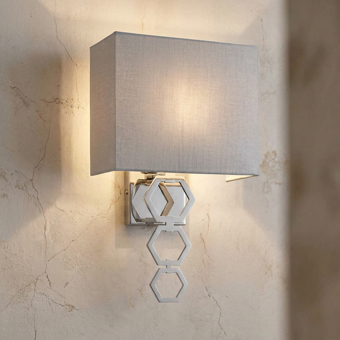 Modern chrome wall light with a grey fabric shade and linked hexagonal rings mounted on a textured wall.