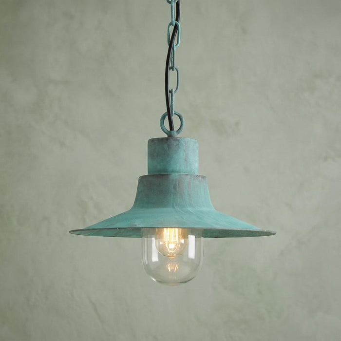 Verdigris outdoor pendant light with a wide metal shade and glass globe hanging against a textured wall.