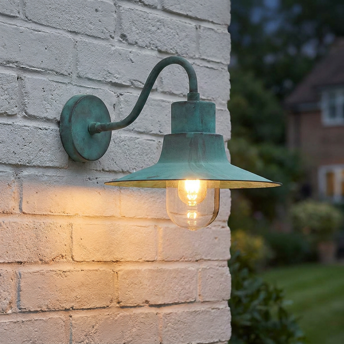 A verdigris outdoor wall light with a glowing bulb mounted on a white brick wall.