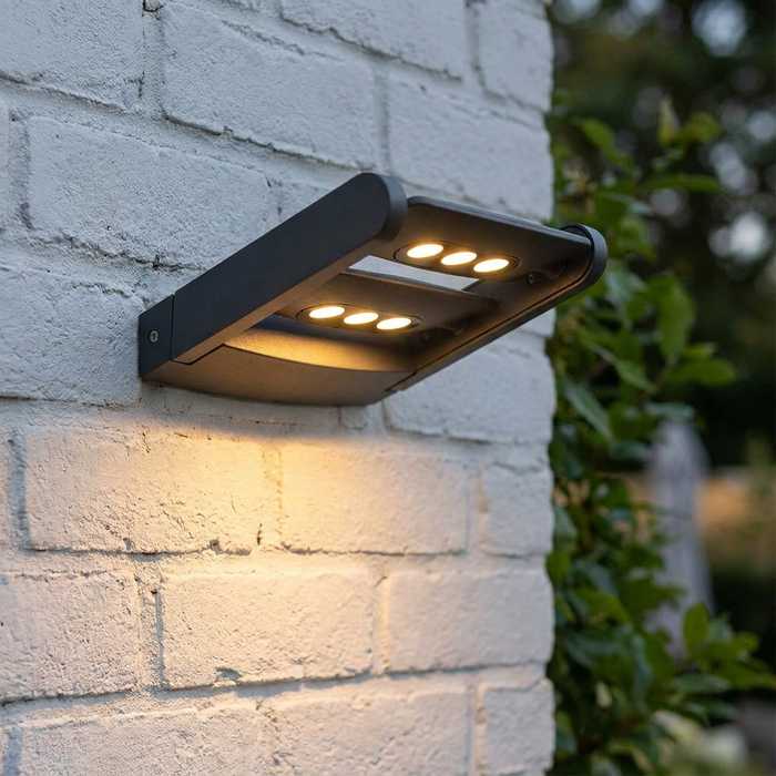 Modern graphite double outdoor wall light illuminating a white brick wall with warm LED panels.
