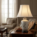 Silver and cream ceramic table lamp with a thistle pattern and white shade on a living room side table.