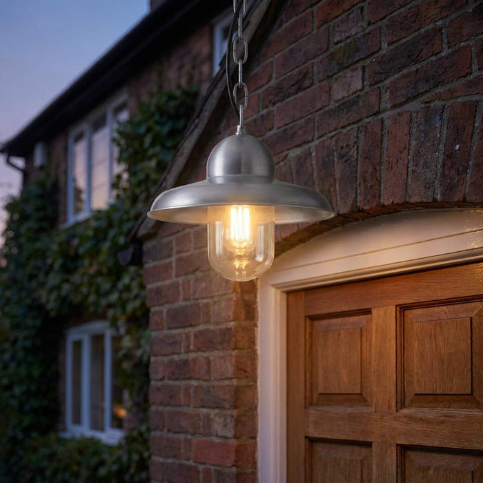 Antique nickel outdoor pendant light with a clear glass shade hanging above a wooden door at dusk.