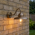 Antique brass outdoor wall light with swan neck arm and clear glass shade illuminated on a yellow brick wall.