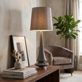 Tall grey ceramic table lamp with a fabric shade on a wooden console table in a modern living room setting.