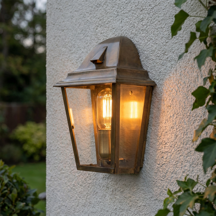Aged brass outdoor wall lantern with a glowing Edison bulb mounted on a white textured exterior wall.