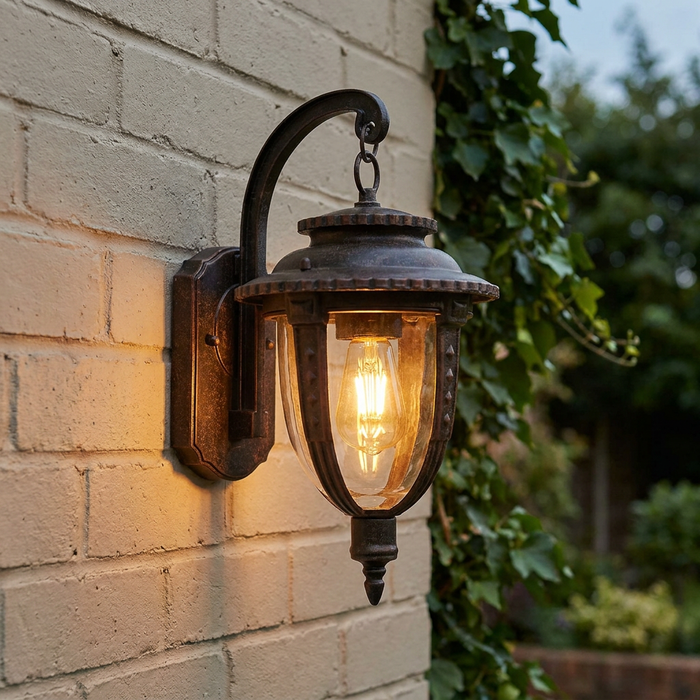 Weathered bronze outdoor lantern with a glowing filament bulb mounted on a light-colored brick wall.