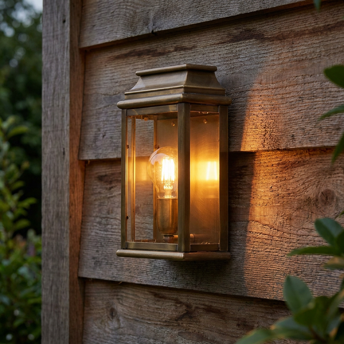 Aged brass outdoor wall lantern with a glowing Edison bulb mounted on a rustic wooden wall.
