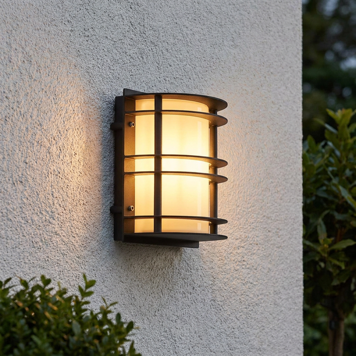Modern black outdoor wall light with horizontal ribs and frosted glass glowing warm on a textured white wall.