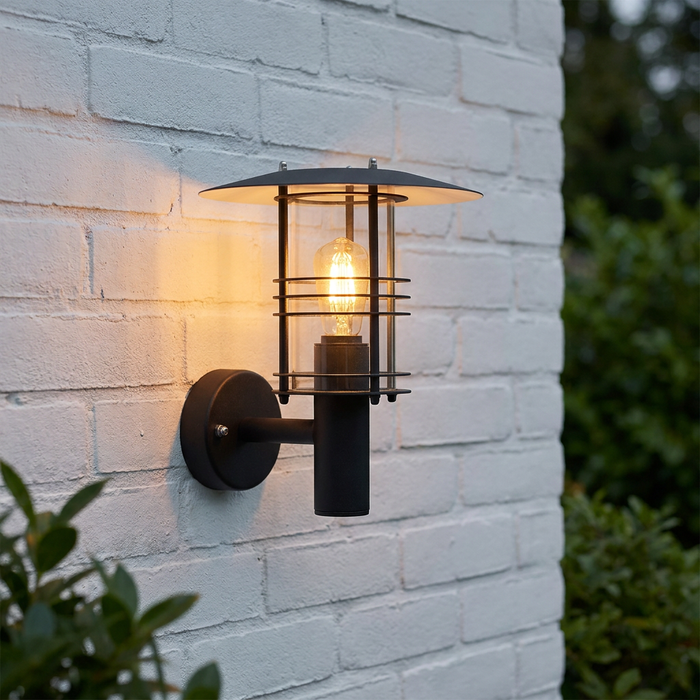 Elstead Stockholm black outdoor wall light with a warm filament bulb mounted on a white brick wall.