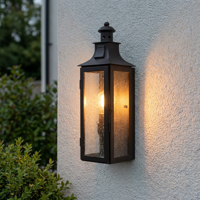 Illuminated Elstead Stow old bronze outdoor wall lantern with seeded glass on a white textured exterior wall.