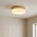 Modern flush mount ceiling light with a gold base and frosted glass shade, illuminated in a minimalist room.
