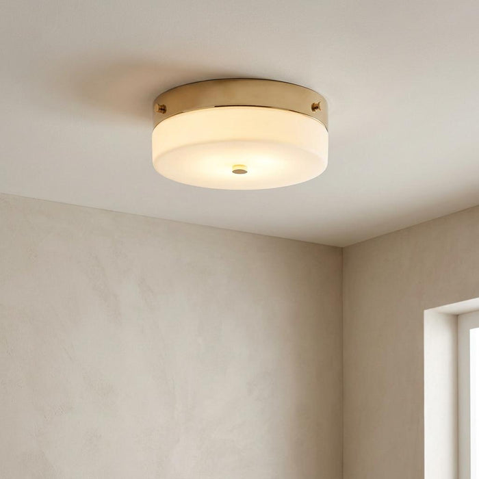 Modern flush mount ceiling light with a gold base and frosted glass shade, illuminated in a minimalist room.