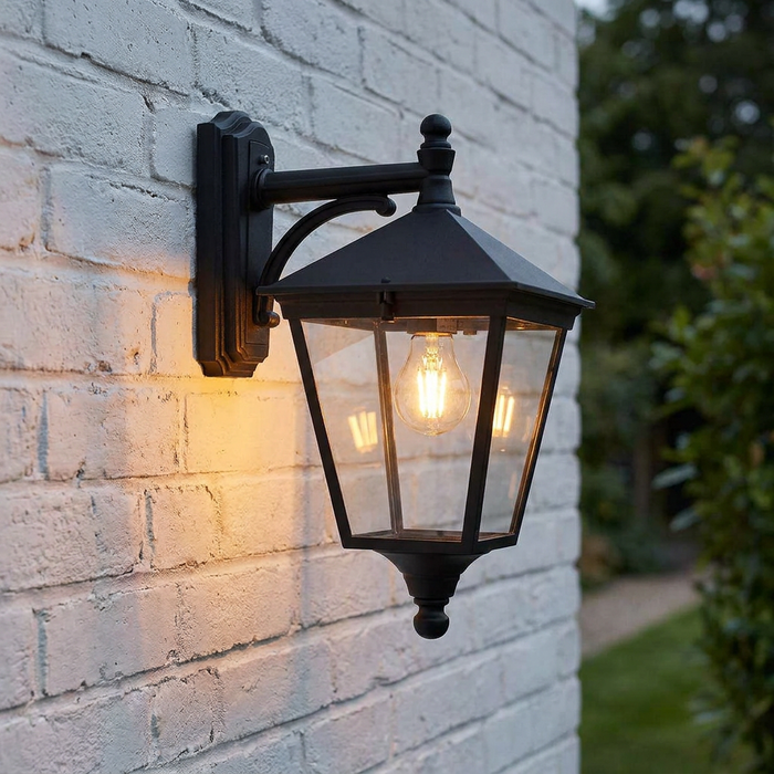 Traditional black lantern wall light with a warm glowing bulb mounted on a white painted brick wall.