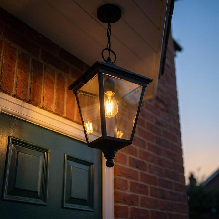 A black lantern outdoor pendant light hanging above a green front door, illuminated at dusk.