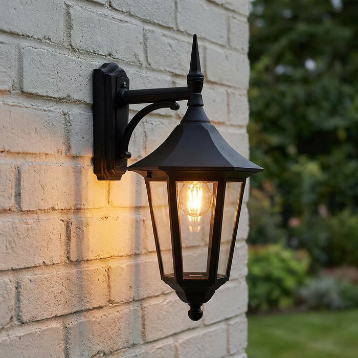 Traditional black outdoor wall lantern with warm glowing bulb mounted on a white brick wall.