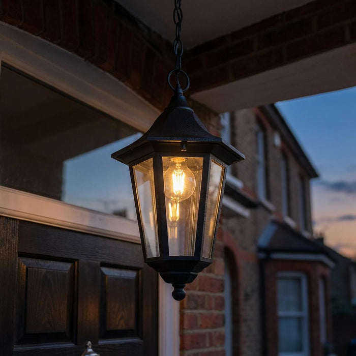Black Valencia lantern-style outdoor pendant light with a warm filament bulb hanging from a porch ceiling.