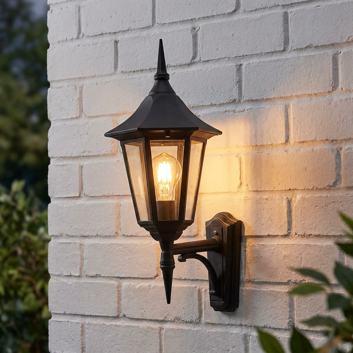 Traditional black lantern-style wall light with a warm bulb mounted on a white brick wall.