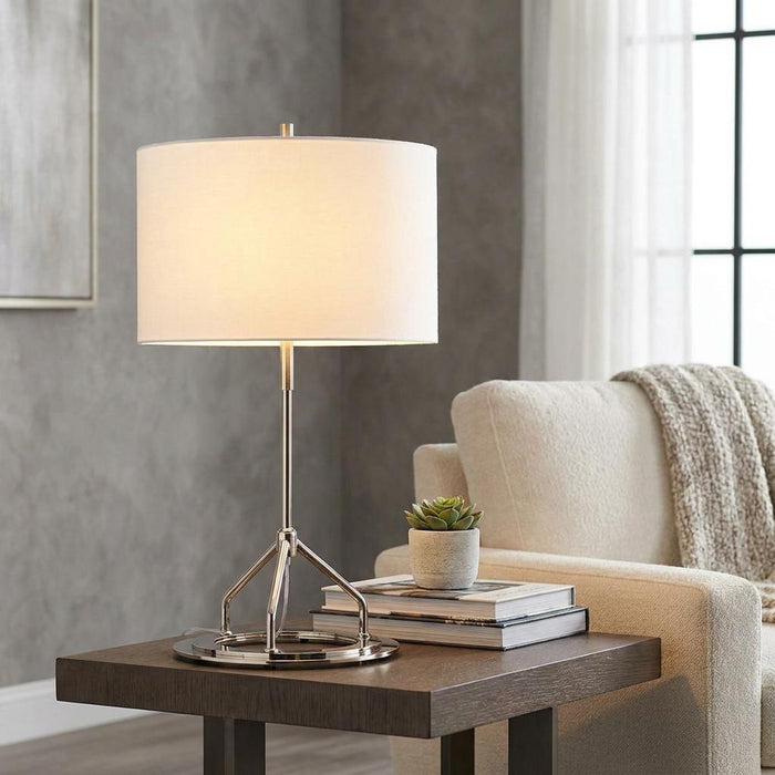 Elstead Vicenza table lamp with a polished nickel tripod base and white drum shade lit on a dark wood side table.