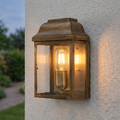 An aged brass outdoor wall lantern with a warm filament bulb mounted on a white textured wall.