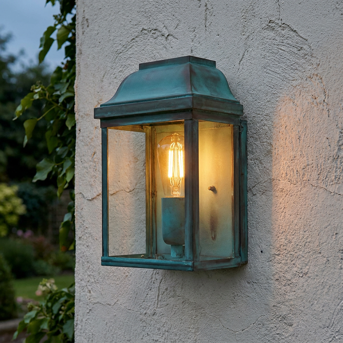 Victorian verdigris outdoor wall lantern with a glowing filament bulb mounted on a textured white wall.