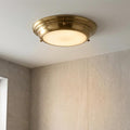 Round brass flush ceiling light with frosted diffuser glowing in a modern tiled bathroom.