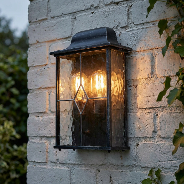 Traditional Elstead Wexford black and silver outdoor wall lantern with leaded glass on a white brick wall.