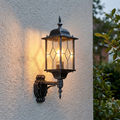 Traditional black and silver lantern wall light with diamond glass panels glowing on a light stucco exterior wall.