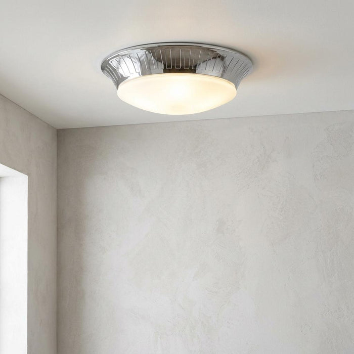 Polished chrome flush mount ceiling light with a frosted glass dome glowing warmly on a white ceiling.