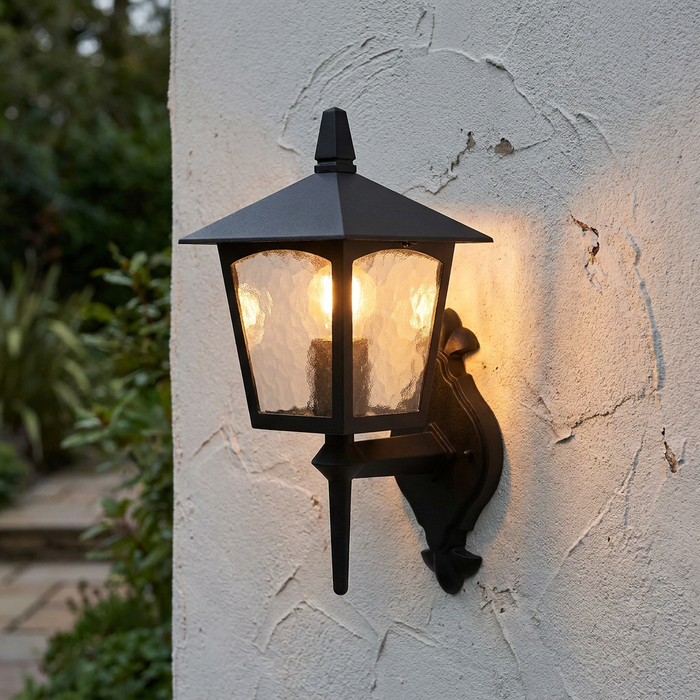 Traditional black lantern outdoor wall light with warm illumination mounted on a textured white wall.