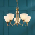 Endon Alton 5 arm antique brass ceiling pendant with white glass shades against a teal paneled wall.
