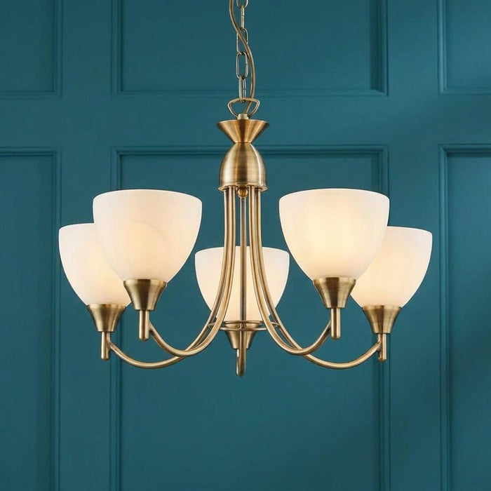 Endon Alton 5 arm antique brass ceiling pendant with white glass shades against a teal paneled wall.