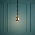 Antique brass pendant light socket with black twisted cord against a teal paneled wall.