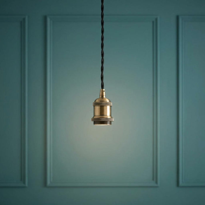 Antique brass pendant light socket with black twisted cord against a teal paneled wall.