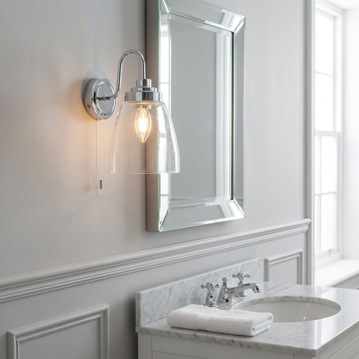 Chrome wall light with a clear glass shade mounted next to a bathroom mirror.