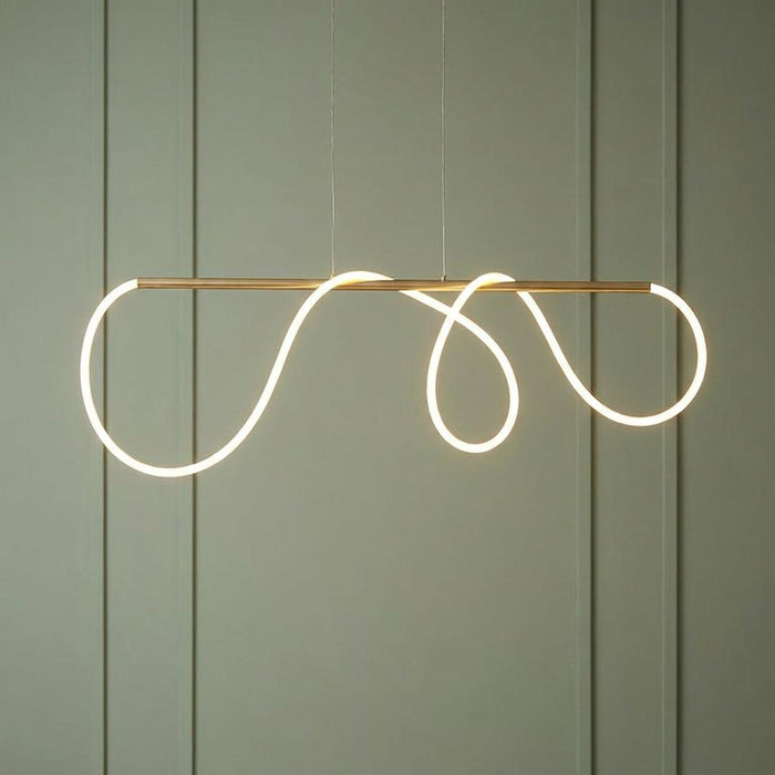 A modern ceiling pendant with a glowing white LED loop wound around a satin gold bar against a green wall.