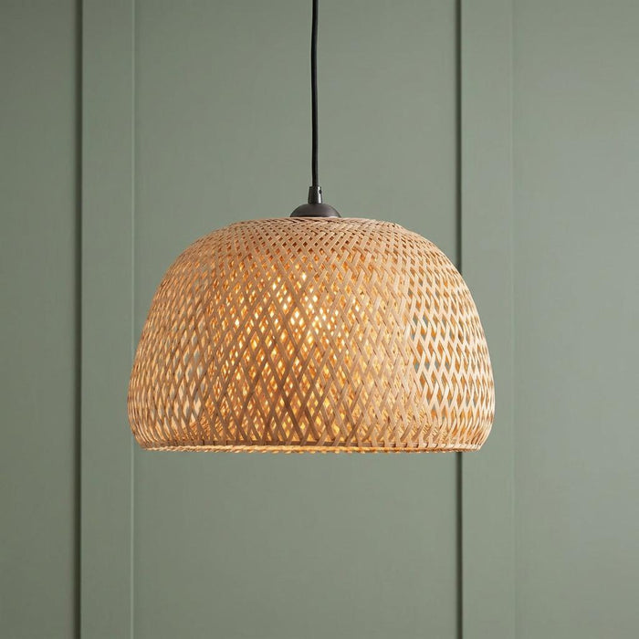Woven bamboo dome pendant light glowing warmly against a sage green paneled background.