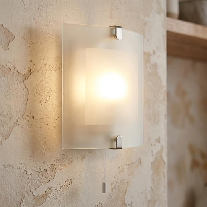 Square frosted glass wall light with chrome clips and a pull cord glowing on a textured beige wall.