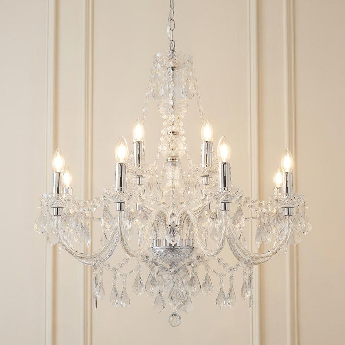 Endon Clarence 12-arm chrome and clear acrylic chandelier with lit bulbs against a neutral paneled wall.