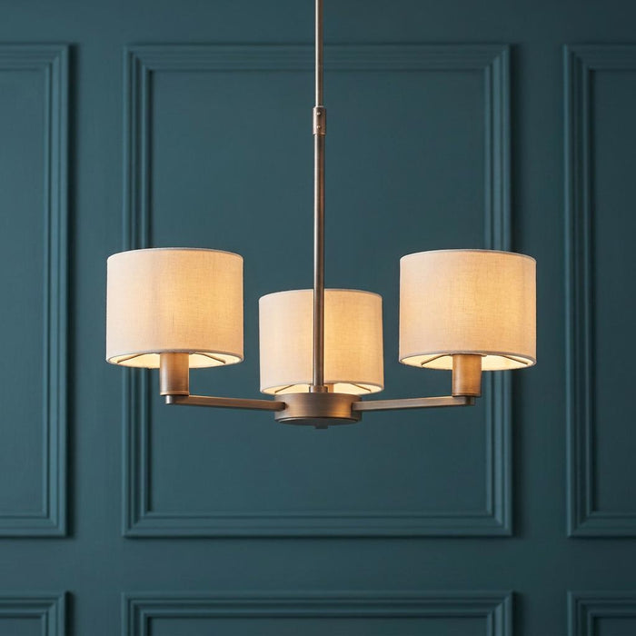 Endon Daley 3-light bronze pendant with beige fabric shades against a teal paneled wall.