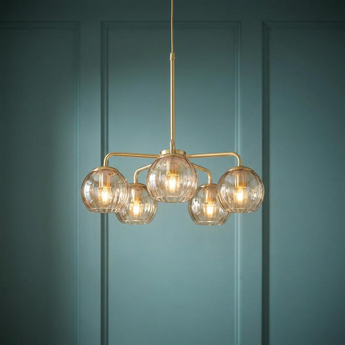 Five-light brass pendant with amber dimpled glass globes hanging against a teal paneled wall.